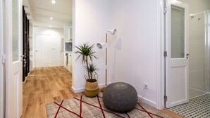 A hallway with a wooden floor, a potted plant, a round ottoman, and a wall-mounted light fixture. - Boho-Chic Santos Apartment: Industriais 7 (Lisbon)