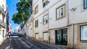 A narrow street with tram tracks, buildings on either side, and a tree in the foreground. - Boho-Chic Santos Apartment: Industriais 7 (Lisbon)