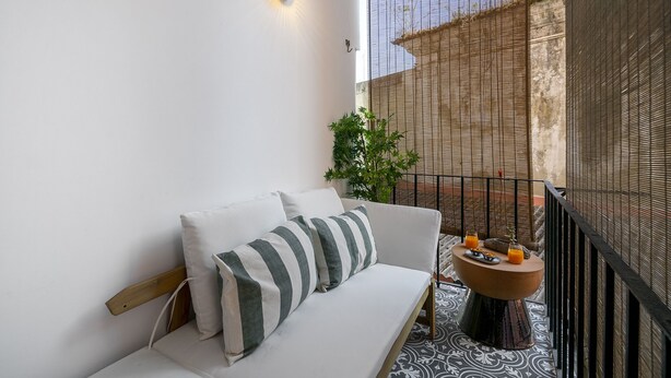 A balcony with a white sofa, striped pillows, a round wooden table with drinks, and a decorative plant. - Premium Alfama 2-Br Great For Remote Workers & Digital Nomads (Lisbon)