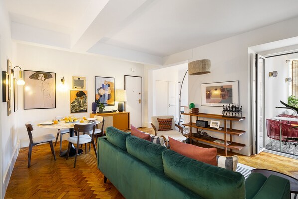 A modern living room with a green sofa, dining table, and artwork on the walls. - Premium Alfama 2-Br Great For Remote Workers & Digital Nomads (Lisbon)