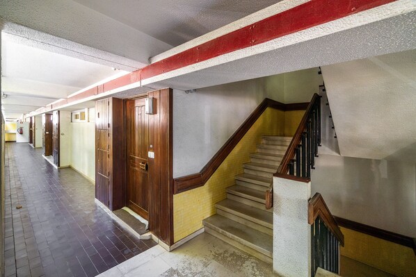 A hallway with wooden doors, a staircase with a wooden handrail, and a tiled floor.