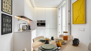 A modern kitchen with white cabinets, a stainless steel range hood, and a yellow abstract painting on the wall.