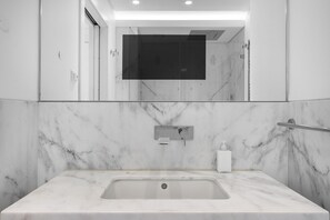 Un bagno moderno con un lavabo in marmo, un soffione a mano e uno specchio grande.