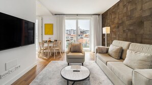 A modern living room with a flat-screen TV, a sofa, a coffee table, and a dining area with chairs and a table.