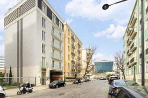 Una strada fiancheggiata da edifici a più piani, con uno scooter parcheggiato e diverse auto.