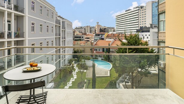 A balcony with a table and chairs, overlooking a swimming pool and a cityscape.