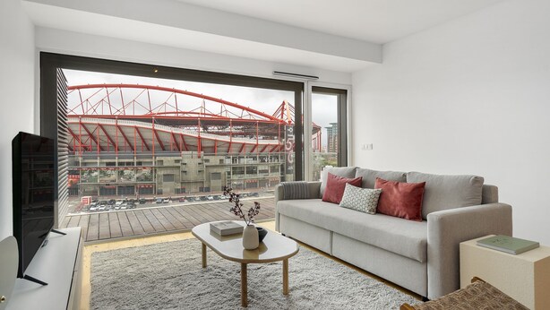 A modern living room with a large window, a grey sofa, a coffee table, and a view of a red bridge outside. - Urban Retreat W/Parking, Elevator & Ac By Benfica Stadium (Lisbon)