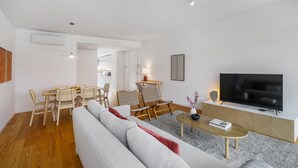 A modern living room with a sofa, dining table, chairs, a TV, and a coffee table. - Urban Retreat W/Parking, Elevator & Ac By Benfica Stadium (Lisbon)