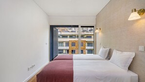 A modern hotel room with a large bed, a red throw blanket, and a view of the cityscape through a large window. - Urban Retreat W/Parking, Elevator & Ac By Benfica Stadium (Lisbon)
