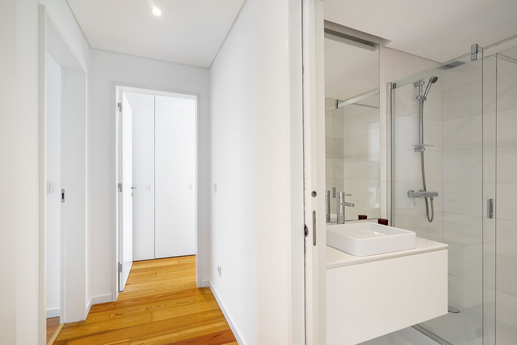 A modern bathroom with a glass shower enclosure, a white sink, and a wooden floor.