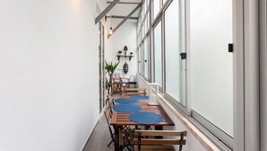 Un pasillo con una larga mesa de madera y sillas, plantas en macetas y lámparas colgantes.