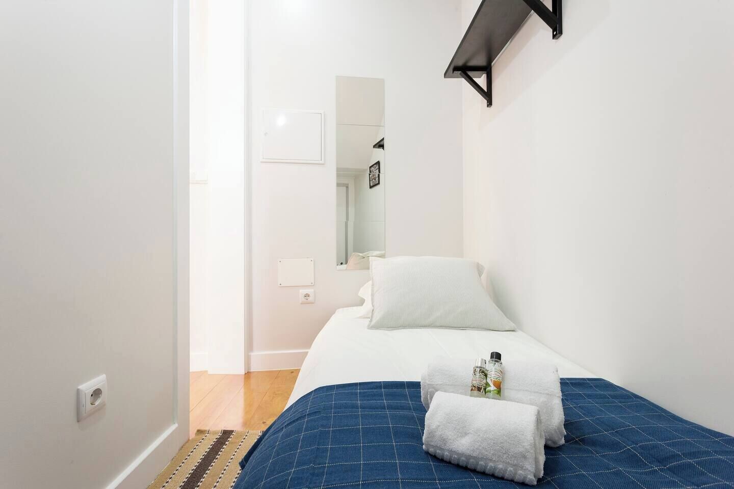 A bedroom with a bed, a blue bedspread, a white pillow, and a towel with a bottle on it.