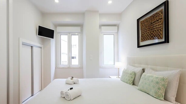 Una habitación de hotel con una cama grande, dos ventanas, un televisor de pantalla plana y una obra de arte enmarcada en la pared.