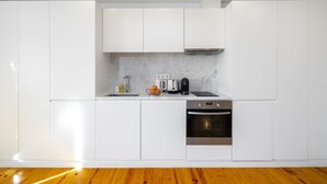 A modern kitchen with white cabinetry, a marble backsplash, a stainless steel oven, and a coffee maker.