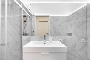 A modern bathroom with a white sink, marble walls, and a glass shower enclosure. - Lisbon'S Best Kept Secret: 2-Bed W/Ac & Patio (Lisbon)