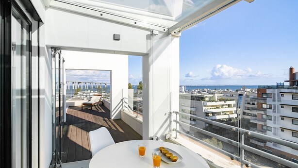Un balcon avec une table, deux verres de jus d’orange et une assiette de pâtisseries.