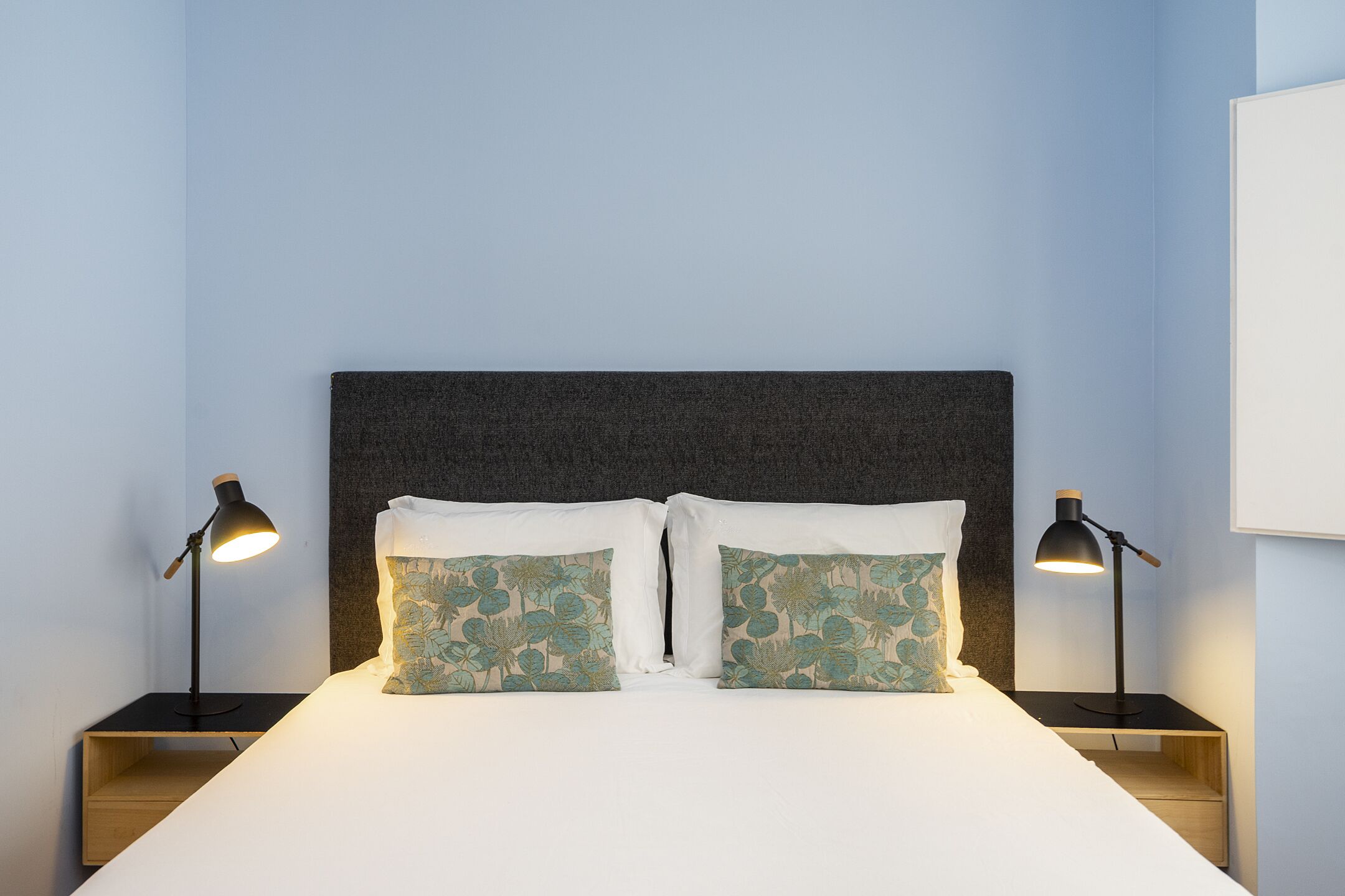 Una cama bien hecha con dos almohadas, dos mesitas de noche y dos lámparas.