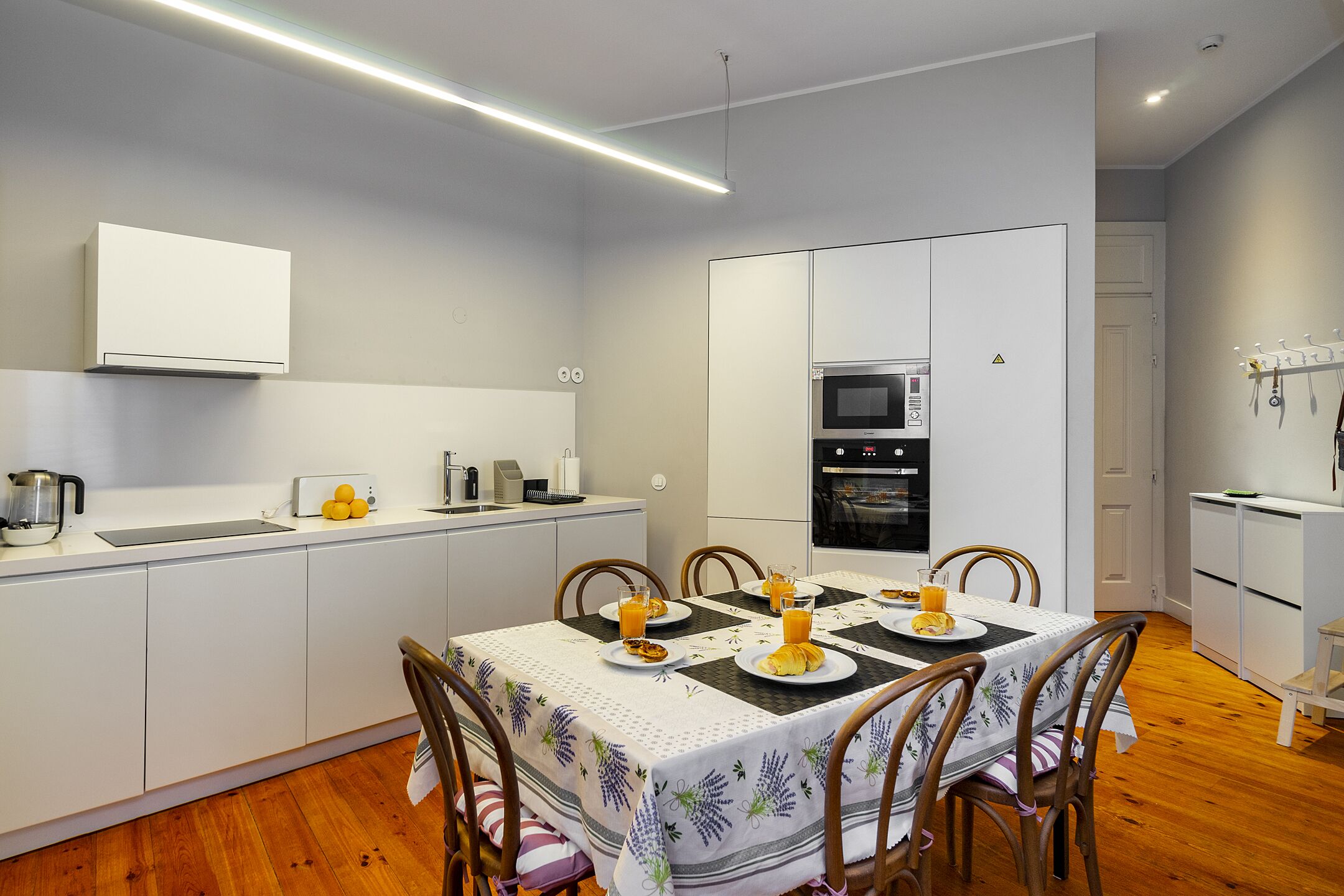 A compact kitchen with white cabinetry, a microwave, and a coffee maker. There is a dining table with chairs and plates of food.