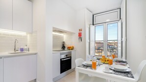 A modern kitchen with white cabinetry, a built-in oven, and a dining area with a table set for breakfast. - Mouraria Modern Living Breathtaking Views & Ac (Lisbon)
