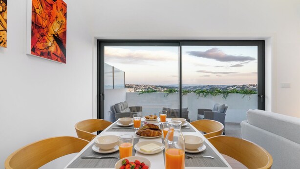 A dining table set with breakfast items, a city view through large windows, and modern furniture. - C314 Riverside View Premium Apartment w/ AC & Terrace (Porto)