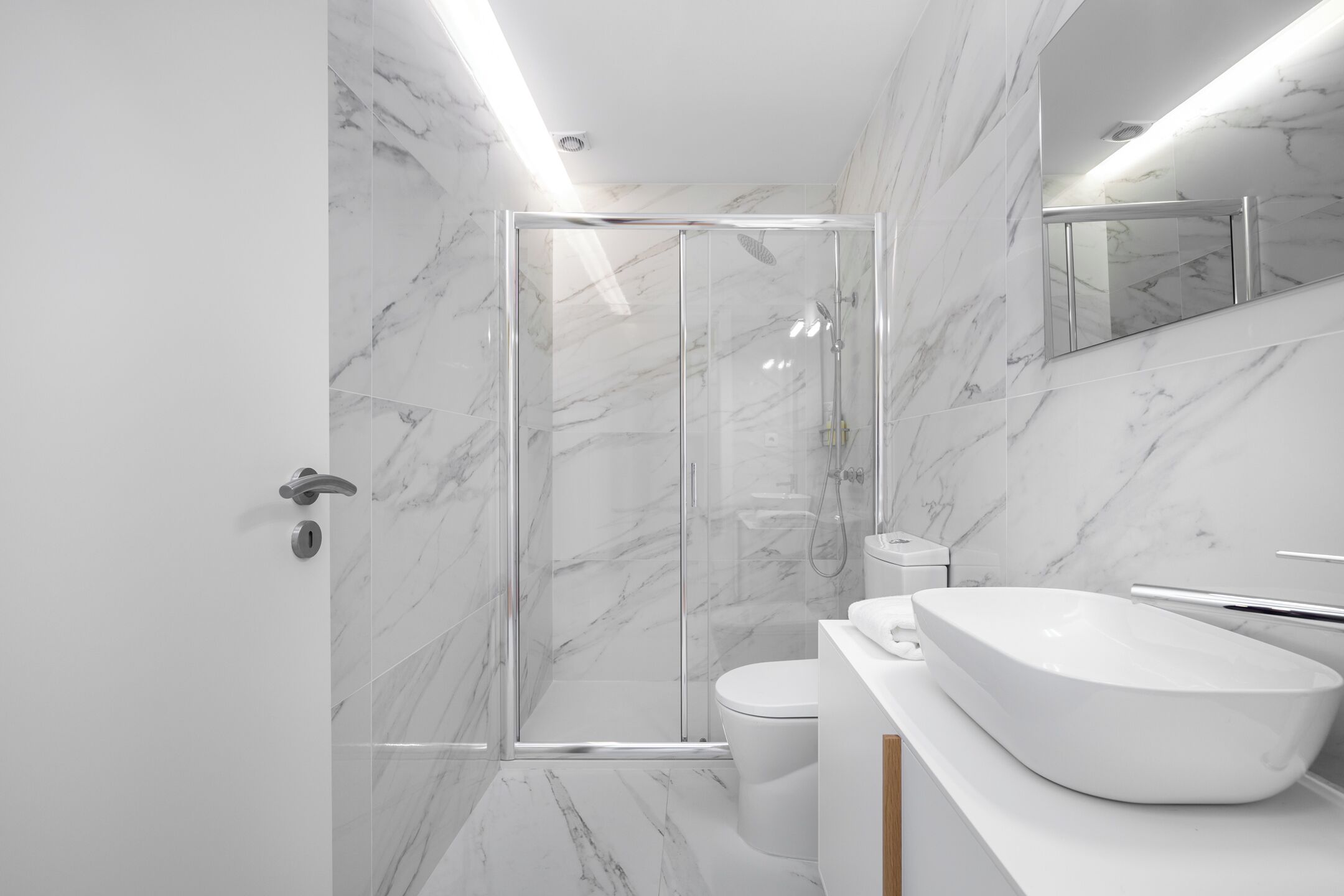 Une salle de bain moderne avec une douche à parois de verre, un lavabo blanc et un mur recouvert de carreaux de marbre.