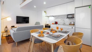 A modern kitchen with white cabinets, a Bosch refrigerator, and a microwave. There is a dining table with chairs and a grey sofa in the living area. - C314 Riverside View Premium Apartment w/ AC & Terrace (Porto)