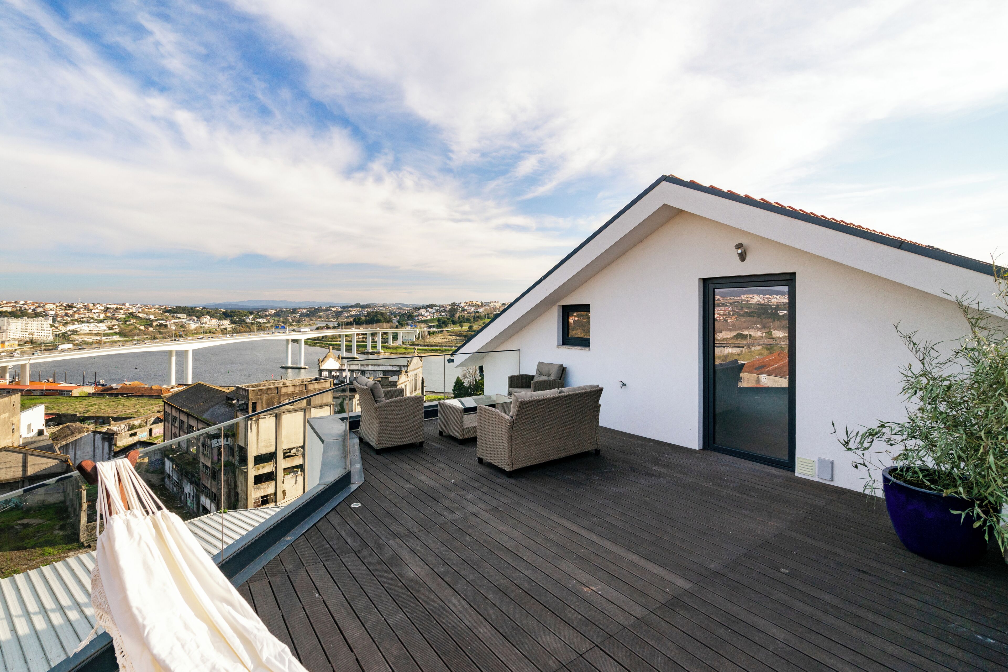 A rooftop terrace with a view of a river and cityscape, furnished with sofas and a hammock.