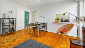 Ein modernes Wohnzimmer mit Holzboden, einem Esstisch mit Stühlen, einem Korbstuhl, einem Laptop und einem Spiegel an der Wand.