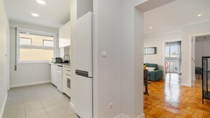 Eine moderne Küche mit weißen Schränken, einem Einbauofen und einem Kühlschrank. Es gibt einen Essbereich mit Tisch und Stühlen sowie einen Balkon mit Aussicht.