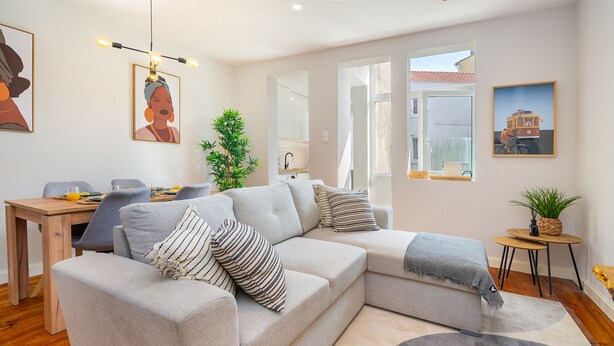 A modern living room with a sectional sofa, a dining table with chairs, a small side table with a plant, and artwork on the walls. - Formosa #2 Central 2-Bed In Prime Location Perfect To Explore Porto (Porto)