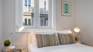 A neatly made bed with striped pillows, a bedside lamp, and a small table with a plant. - Formosa #2 Central 2-Bed In Prime Location Perfect To Explore Porto (Porto)