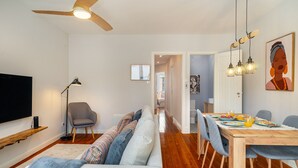 Ein modernes Wohnzimmer mit Sofa, einem Esstisch mit Stühlen, einem Fernseher und einem Deckenventilator.