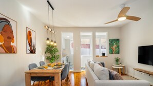 Ein modernes Wohnzimmer mit einer Couch, einem Esstisch und Stühlen. Ein Fernseher ist an der Wand montiert und ein Deckenventilator ist vorhanden.