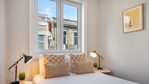Ein Schlafzimmer mit einem Bett, zwei Nachttischen, einem Fenster und einem gerahmten Bild an der Wand.