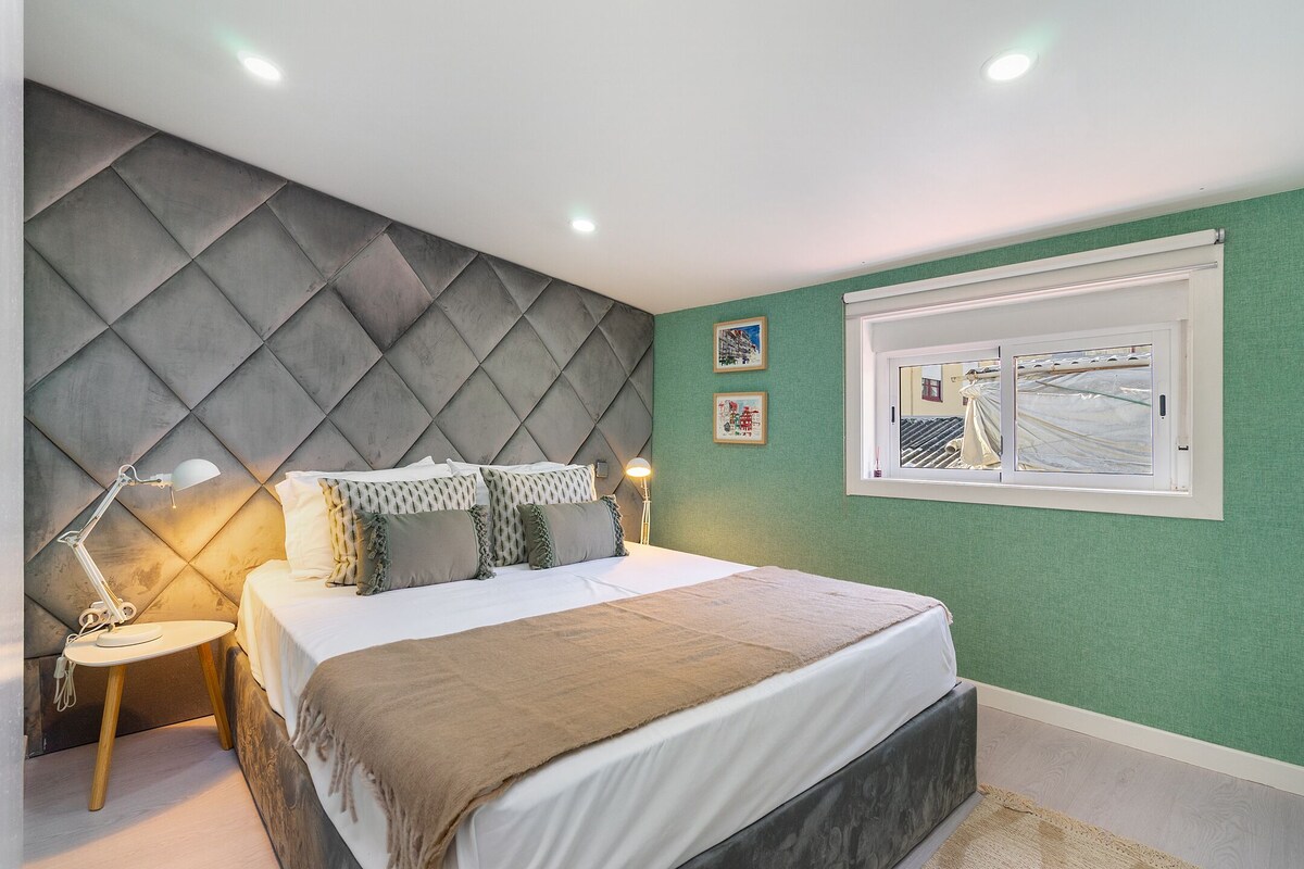 Une chambre à coucher avec un lit, une table de chevet, une lampe, une fenêtre donnant sur un beau paysage et un mur vert.