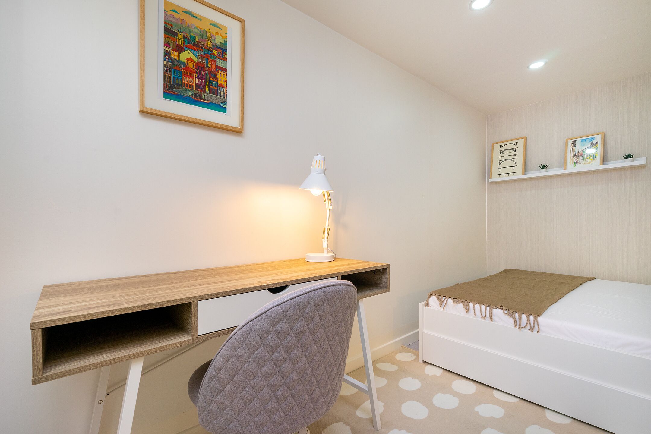 A bedroom with a bed, a desk, a chair, and a lamp.