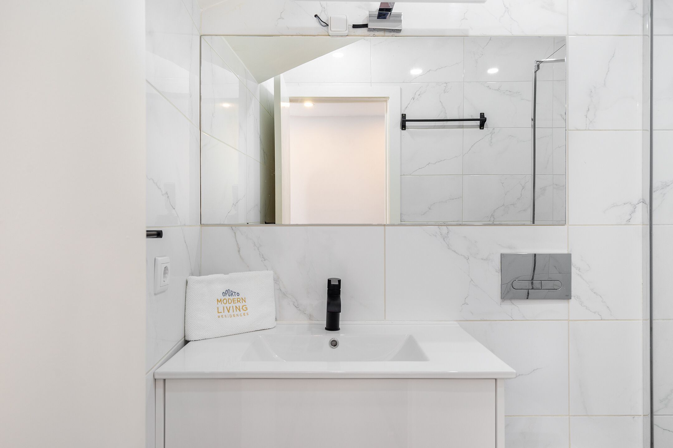 Een moderne badkamer met een witte wastafel, een spiegel en een handdoekhouder.