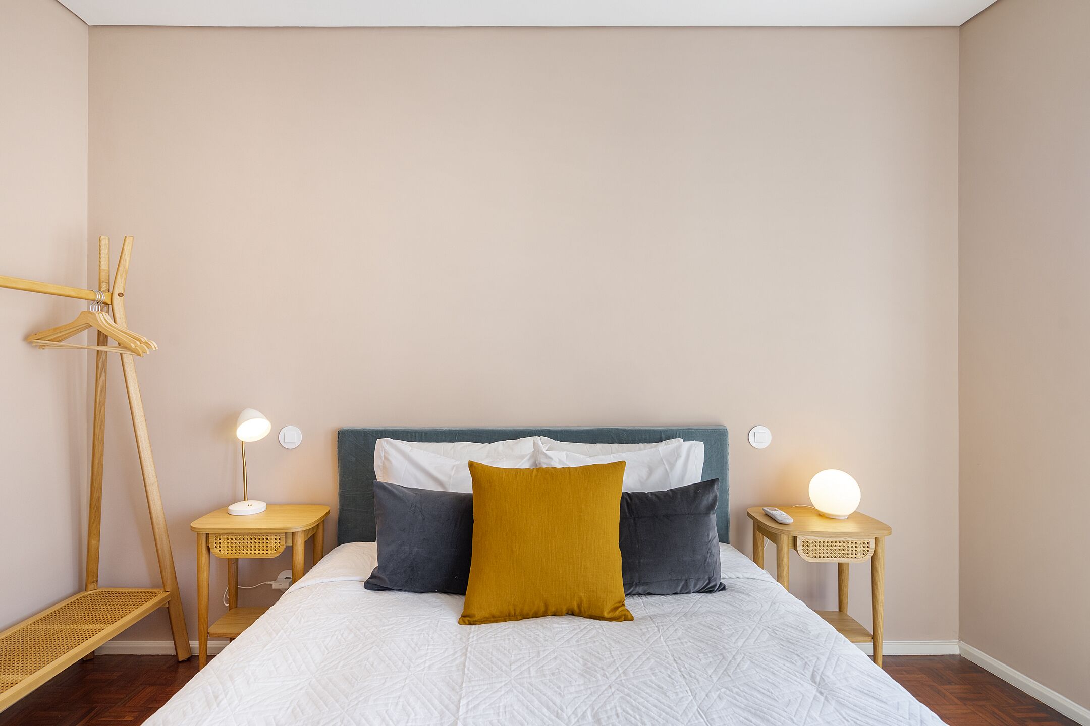 A neatly arranged bedroom with a bed, two bedside tables, a hanging rack, and a wall-mounted light fixture.