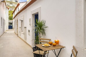 Une rue étroite où une table est dressée pour le petit-déjeuner, avec une assiette de nourriture et des boissons, ainsi qu’une plante en pot.