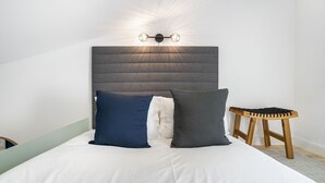 Ein Schlafzimmer mit einem Bett, einem Kopfteil mit einer Lampe und einem hölzernen Hocker.