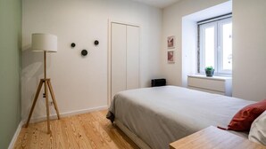A bedroom with a bed, a lamp, a radiator, a window, and a door.