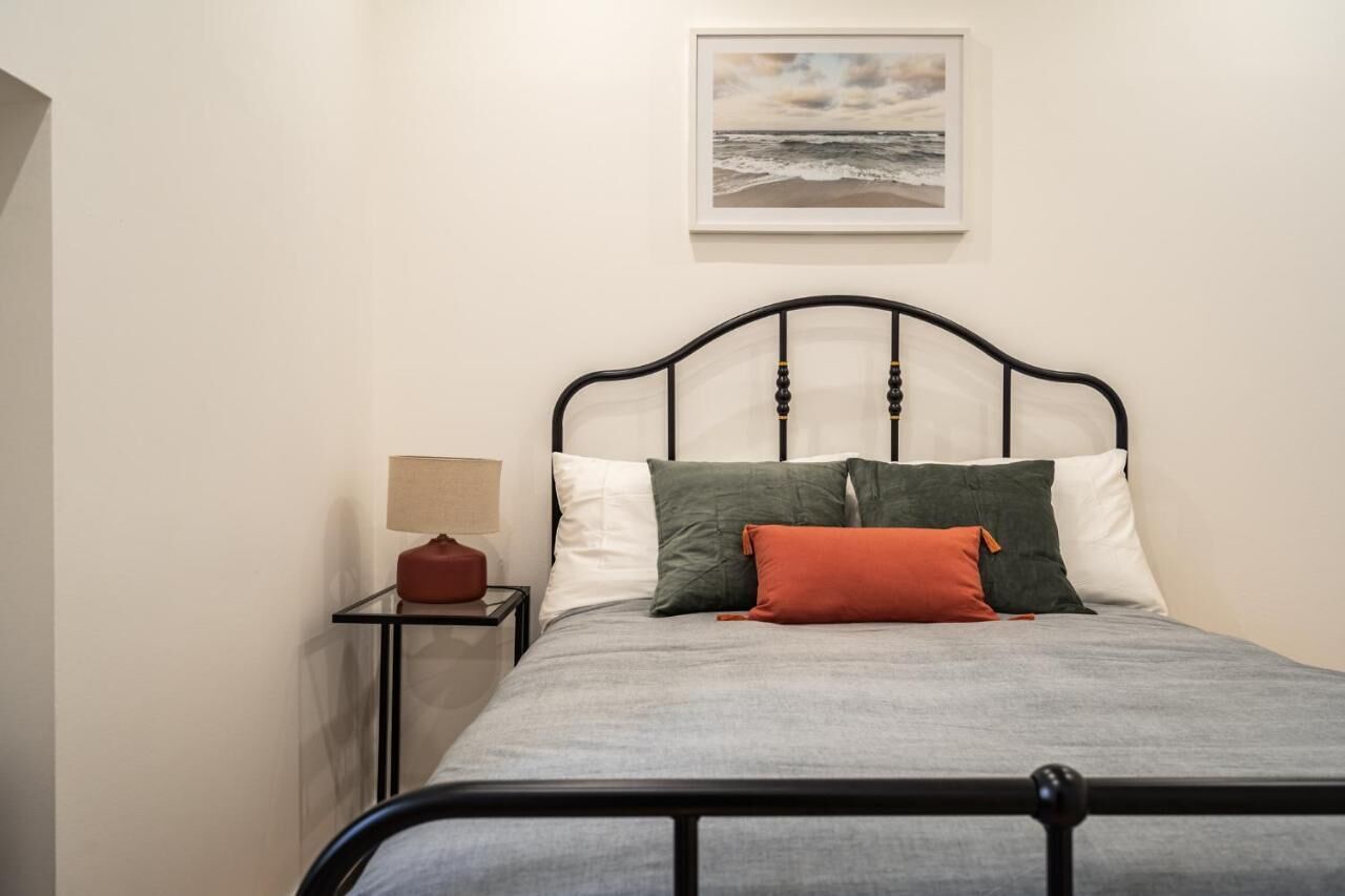 A bed with a grey bedspread, a black metal frame, and multiple pillows in various colors.
