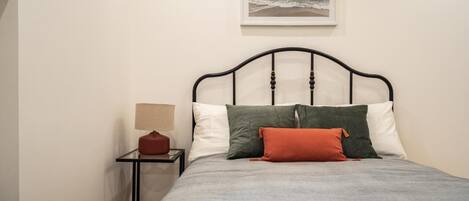 A bed with a grey bedspread, a black metal frame, and multiple pillows in various colors.