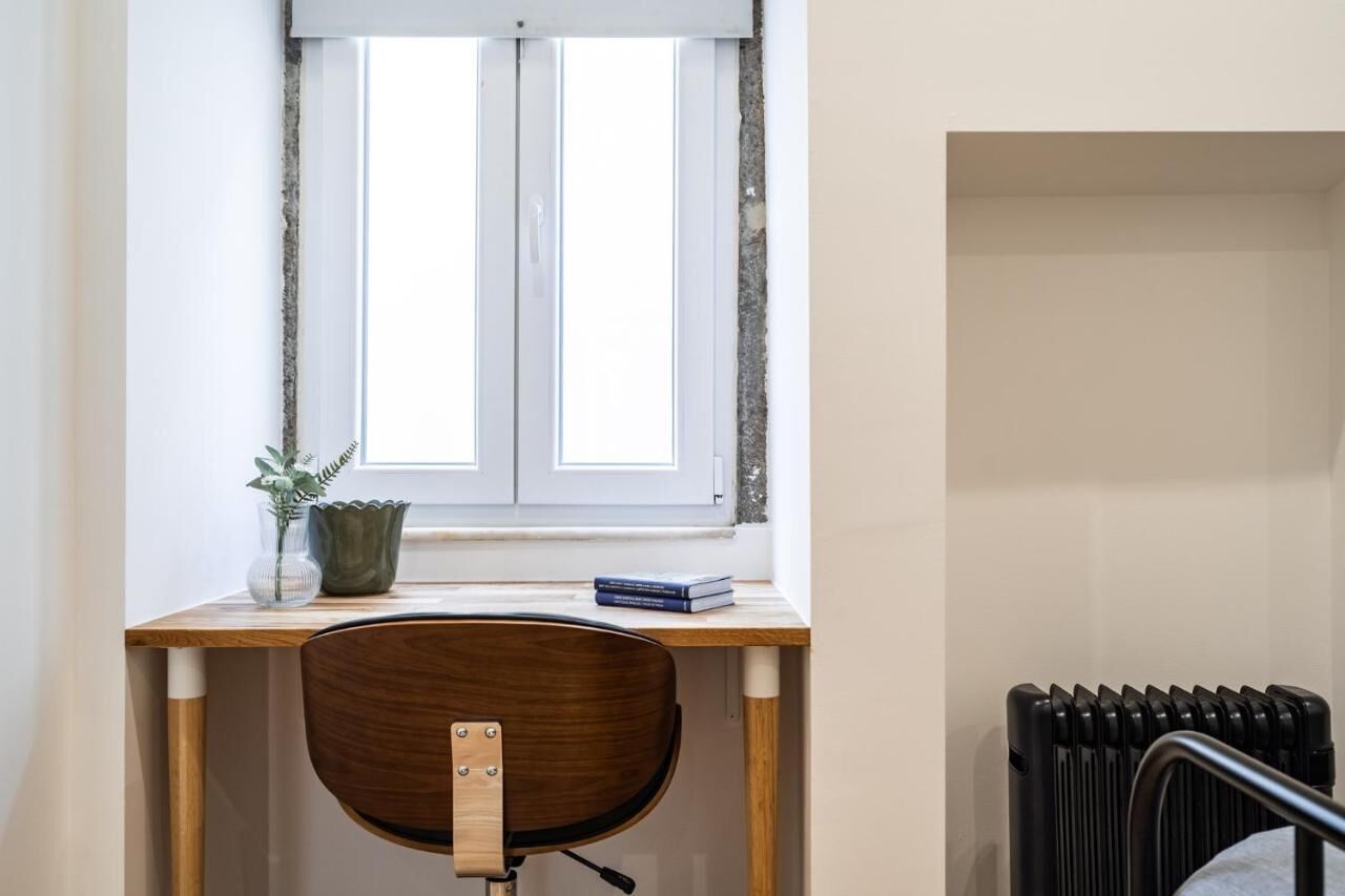 Habitació amb escriptori de fusta, una cadira, un radiador i una finestra amb cortines.