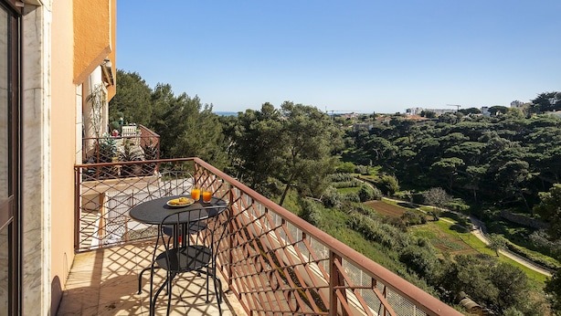 Un balcón con mesa y sillas, con vistas a un paisaje exuberante y edificios lejanos.