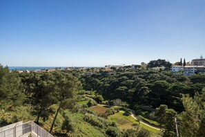 A coastal landscape with dense greenery, a clear sky, and buildings in the distance. - Perfect Family Hideout Residence W/Ac & 4Br + 5Ba (Cascais)