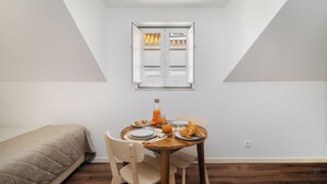 A small, well-lit room with a dining table set for two, a bed, and a window with curtains. - Alfama Studio Prime Location Explore Lisbon W/ Style (Lisbon)