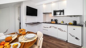 A modern kitchen with white cabinets, a flat-screen TV, and a dining area with a wooden table set for breakfast. - Alfama Studio Prime Location Explore Lisbon W/ Style (Lisbon)