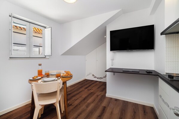 Una cocina moderna con comedor, televisor montado en la pared y una mesa de madera dispuesta con platos y vasos.