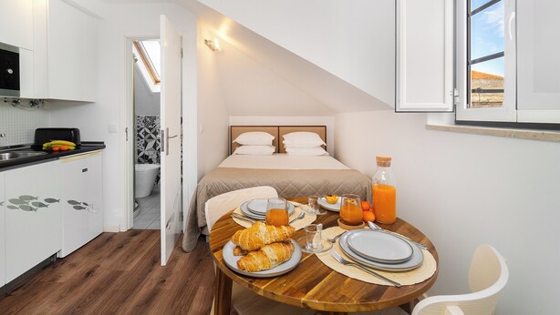 A compact hotel room with a kitchenette, a bed with a view, breakfast setup, and a small dining area. - Alfama Studio Prime Location Explore Lisbon W/ Style (Lisbon)